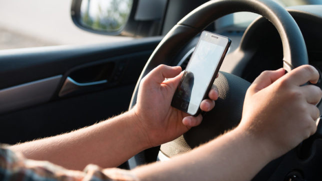 Student shown using phone while sitting behind the wheel of a car. Photo courtesy: newsx.com